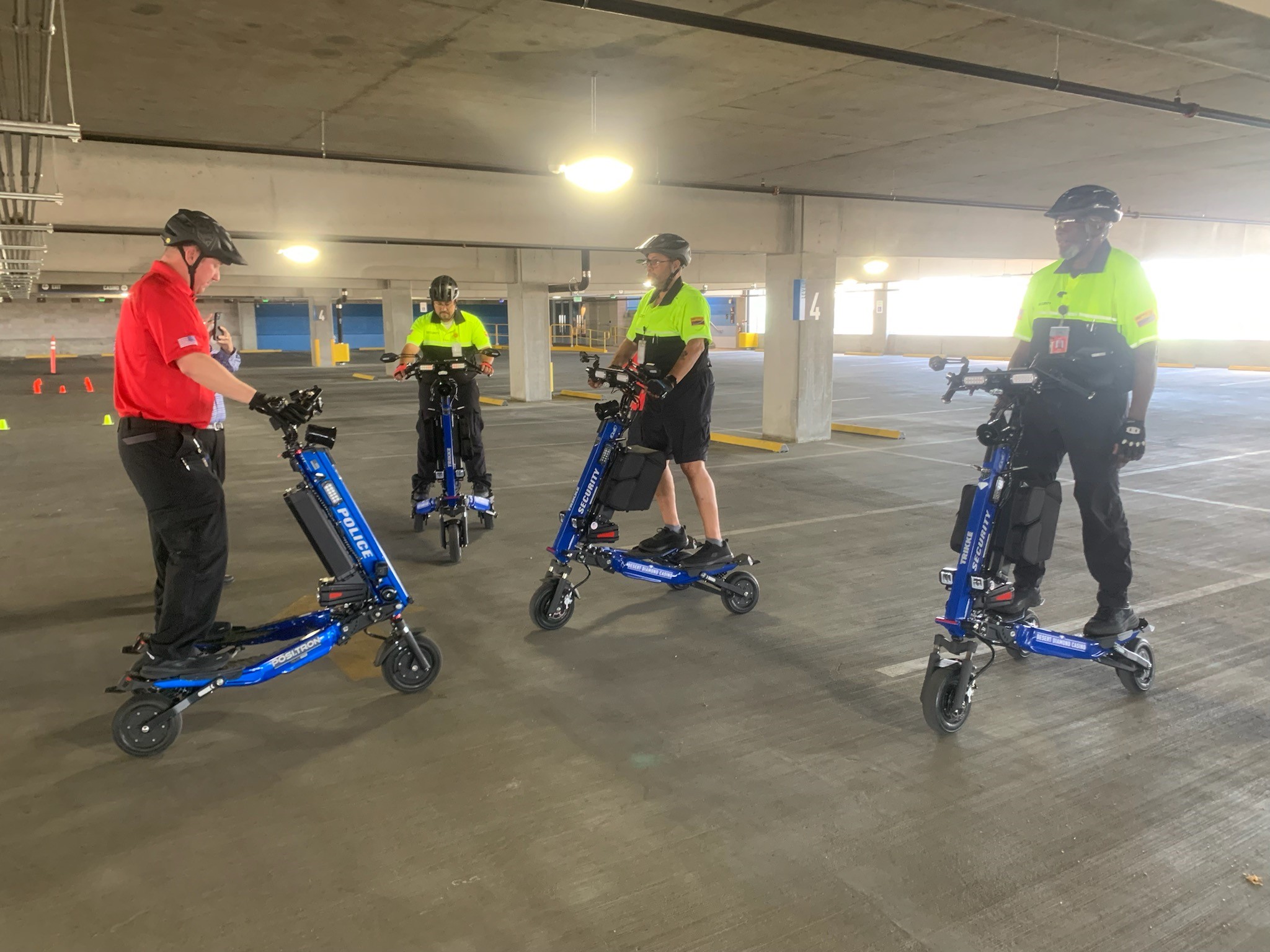 Group of four people on blue Segways in a dim parking garage wearing helmets one person in red shirt appears to lead a briefing