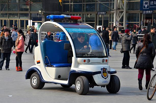Small white police patrol vehicle with blue seating and a red-blue light bar in a crowded public square.