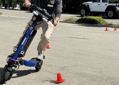 Person wearing a helmet rides a blue electric scooter through orange cones in a parking lot focused on the course ahead