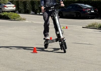 Man wearing a helmet rides a self balancing scooter through orange cone markers in a parking lot with trees and cars in the background